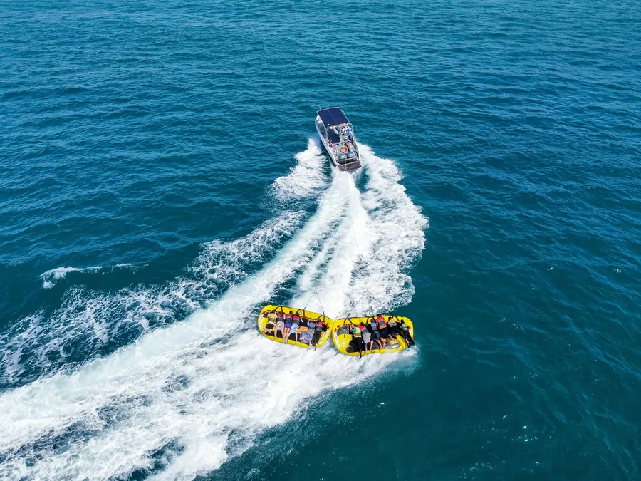 People riding a towed inflatable sofa on the water behind a boat at a beach water activity