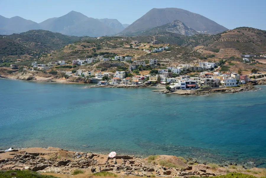 Aerial view of Mochlos seaside village with houses by the water and mountains behind